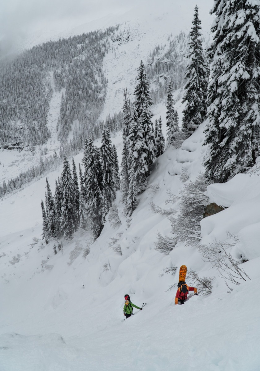 two snowboarders booting up steep snow 1