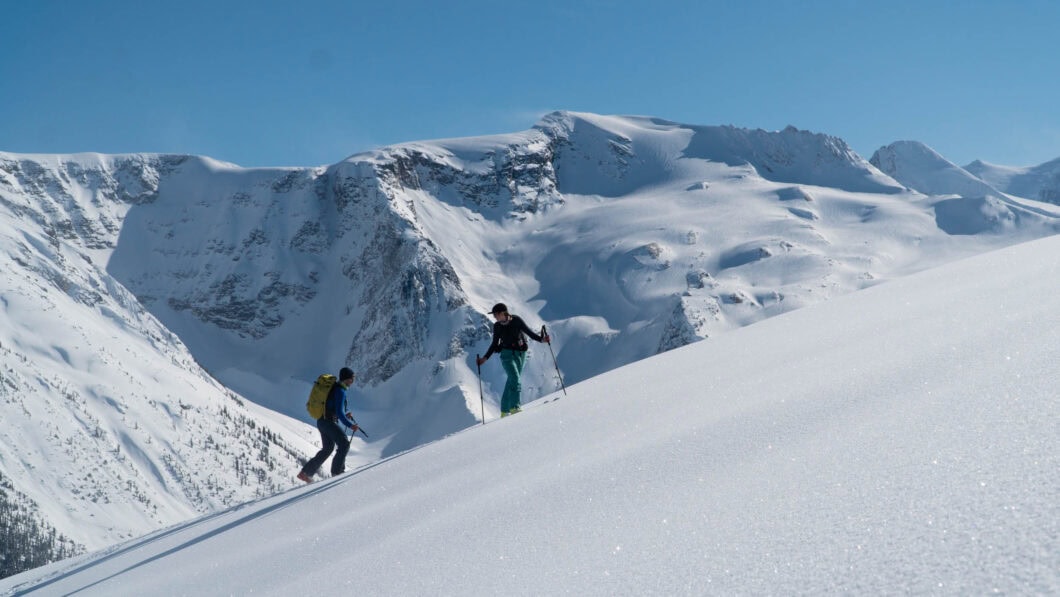 two skiers ascending wintery slopes of the abbott east slidepath