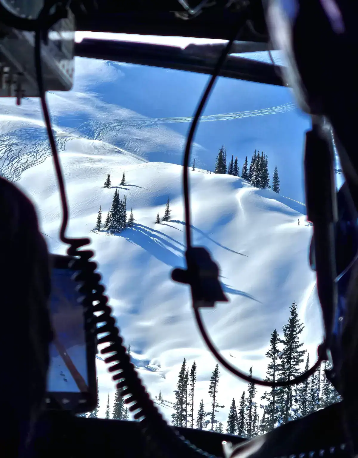 view from inside helicopter looking at ski terrain